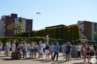Uczestnicy festynu na placu, nad ich głowami model samolotu latającego.